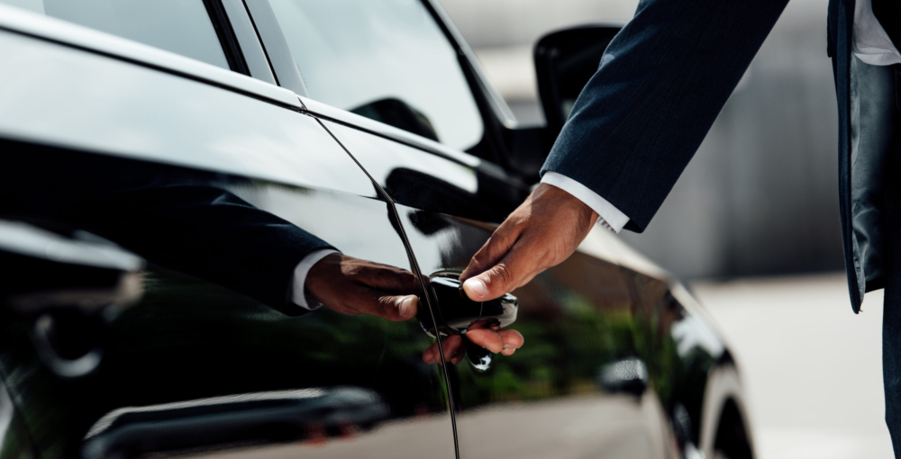 cropped view of african american businessman in suit opening car door at sunny day